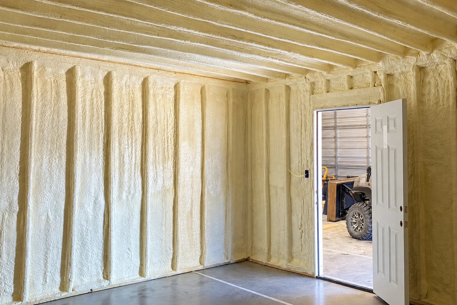 Closed-cell spray foam covers the walls and ceiling of a garage with an open doorway.