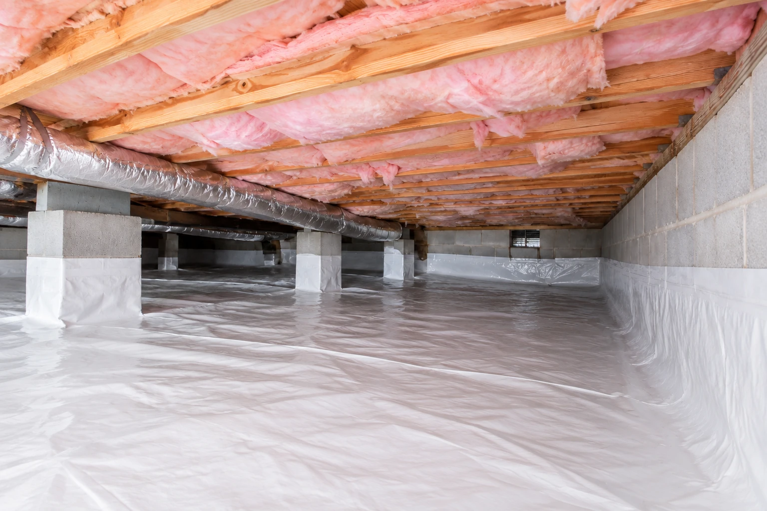 Crawl space with pink insulation between the floor joists, a silver duct, and white plastic vapor barrier covering the ground and support columns.